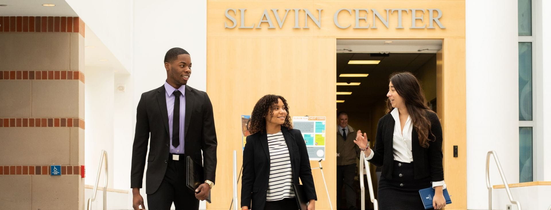 three students in suits walking in atrium